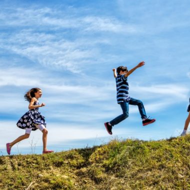 tre børn løber lystigt op af en græsklædt bakke