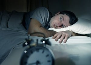 Mand ligger søvnløs i sin seng med vækkeur foran sig